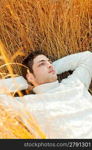 Autumn winter man portrait lying in golden grass field with turtleneck sweater