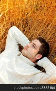 Autumn winter man portrait lying in golden grass field with turtleneck sweater