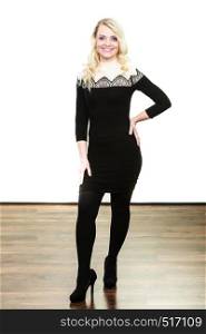 Autumn winter outfit concept. Mid adult blond attractive woman in full length wearing stylish elegant black dress high heels posing, studio shot, wide angle view. Mid aged woman in stylish black dress