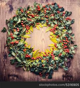 Autumn Wreath of fall leaves and red berries on wooden rustic background, top view
