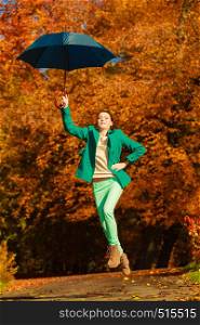 Autumnal fashion concept. Woman walking in park during golden autumn weather, enjoying nature jumping with umbrella having fun.. Woman jumping with umbrella in park during autumn