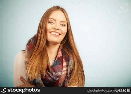 Autumnal outfit concept. Positive smiling young long haired woman wearing warm autumn clothing woolen checked scarf on blue. Woman wearing woolen checked scarf warm autumn clothing