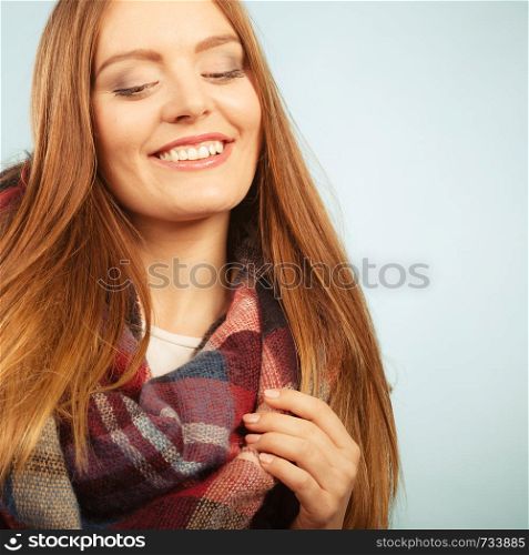 Autumnal outfit concept. Positive smiling young long haired woman wearing warm autumn clothing woolen checked scarf on blue. Woman wearing woolen checked scarf warm autumn clothing