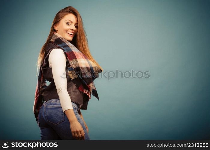 Autumnal outfit concept. Positive smiling young woman wearing warm autumn clothing woolen checked scarf posing on blue. Positive girl in autumn season clothing