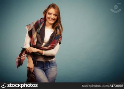 Autumnal outfit concept. Positive smiling young woman wearing warm autumn clothing woolen checked scarf posing on blue. Positive girl in autumn season clothing