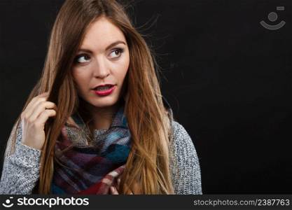 Autumnal outfit concept. Smiling female long hair wearing warm autumn clothing plaid woolen scarf, on dark. Smiling girl wearing warm wooden scarf