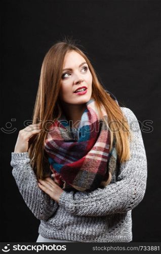 Autumnal outfit concept. Smiling female long hair wearing warm autumn clothing plaid woolen scarf, on dark. Smiling girl wearing warm wooden scarf