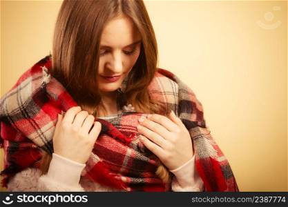 Autumnal outfit concept. Young long haired woman wearing warm autumn clothing woolen checked scarf on beige, studio shot. Woman wearing woolen checked scarf warm autumn clothing