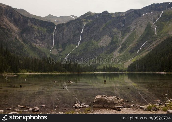 Avalanche Lake in Glacier National Park. The headwall of the valley is in the background with several waterfalls that are cascading down the cliffs from glaciers above.