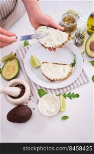 Avocado and cream cheese toasts preparation - Woman smearing cheese on a grilled or toasted bread.. Avocado and cream cheese toasts preparation - Woman smearing cheese on a grilled or toasted bread