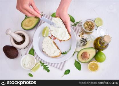 Avocado and cream cheese toasts preparation - Woman smearing cheese on a grilled or toasted bread.. Avocado and cream cheese toasts preparation - Woman smearing cheese on a grilled or toasted bread