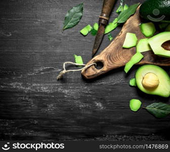 Avocado and knife on the Board. On a black wooden background.. Avocado and knife on the Board.