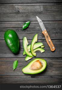 Avocado and small slices of avocado with a knife. On a wooden background.. Avocado and small slices of avocado with a knife.