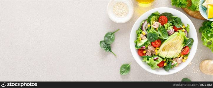 Avocado and tuna fresh vegetable salad with tomato, cucumber corn, onion, lettuce and spinach. Healthy and detox food concept. Ketogenic diet. Buddha bowl dish on light background. Top view. Banner.