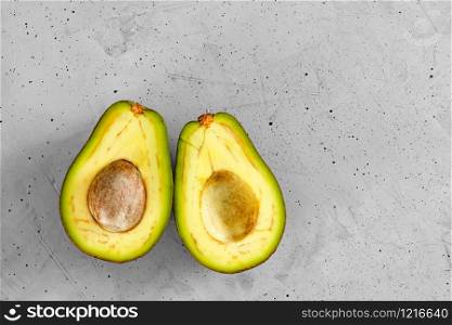 Avocado cut in half, one slice with core on gray concrete background, close-up. Delicious and nutritious fruit, image with copy space.. Two slices of avocado cut in half, one slice with core on gray concrete background, top view.