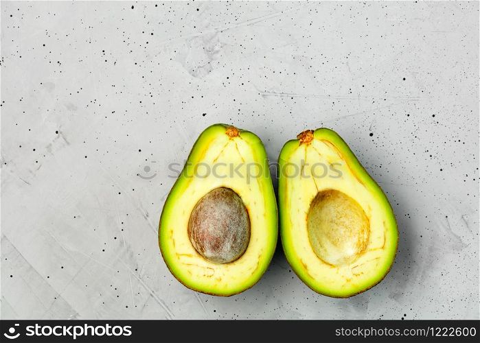 Avocado cut in half, one slice with core on gray concrete background, close-up. Delicious and nutritious fruit, image with copy space.. Two slices of avocado cut in half, one slice with core on gray concrete background, top view.