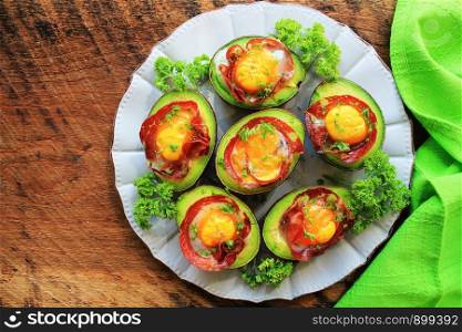 Avocado Egg Boats with bacon on dark wooden background. Top view