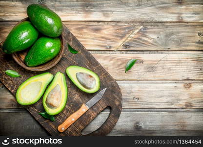 Avocado in a bowl on a black chopping Board with a knife. On a wooden background.. Avocado in a bowl on a black chopping Board with a knife.