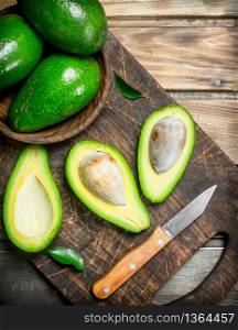 Avocado in a bowl on a black chopping Board with a knife. On a wooden background.. Avocado in a bowl on a black chopping Board with a knife.