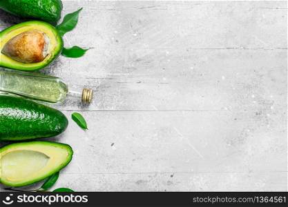 Avocado oil and avocado with leaves. On white rustic background.. Avocado oil and avocado with leaves.