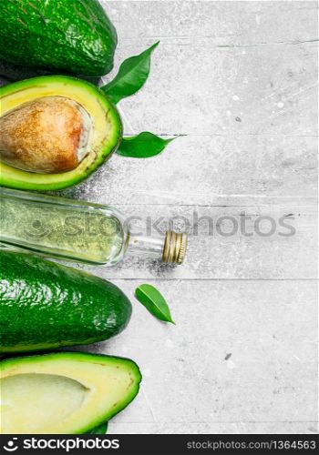 Avocado oil and avocado with leaves. On white rustic background.. Avocado oil and avocado with leaves.