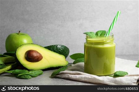 Avocado spinach and green apple smoothie healthy and refreshing tropical drink front view of a glass jar with mint leaves and sliced avocado fruit, apple and spinach leaves on a grey kitchen board with copy space.