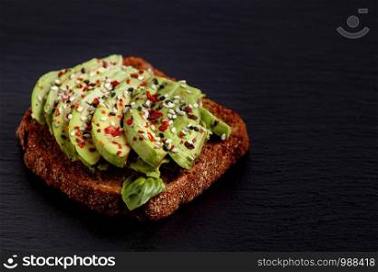 Avocado toast. Vegan sandwich. Healthy food lunch recipe. Light gourmet organic spread. Balanced fitnes meal on black slate board. Diet snack with chili, basil for brunch. Foodie appetizer. Avocado toast. Vegan sandwich healthy lunch recipe