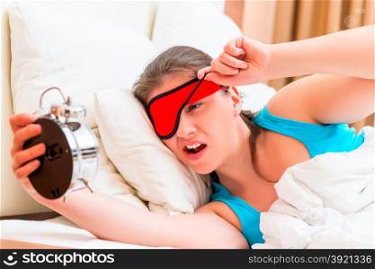 awakened girl looks at an alarm clock with contempt