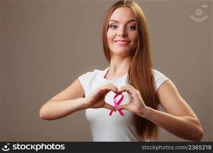 Awareness of breast cancer.Young woman making heart shape by hands on pink ribbon symbol sign. Help and charity. Gray background. Breast cancer. Woman making heart shape on pink ribbon