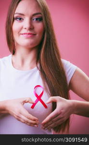 Awareness of breast cancer.Young woman making heart shape by hands on pink ribbon symbol sign. Help and charity. Light red background. Breast cancer. Woman making heart shape on pink ribbon