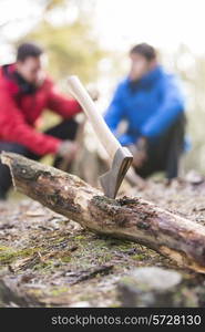 Axe stuck in log with male hikers in background at forest