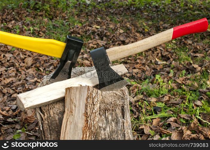 Axes with yellow and wooden handle stuck in old stump on autumn dry leaves background