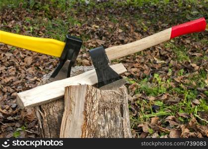 Axes with yellow and wooden handle stuck in old stump on autumn dry leaves background
