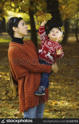 Baby and mother are playing together with fallen leaves.