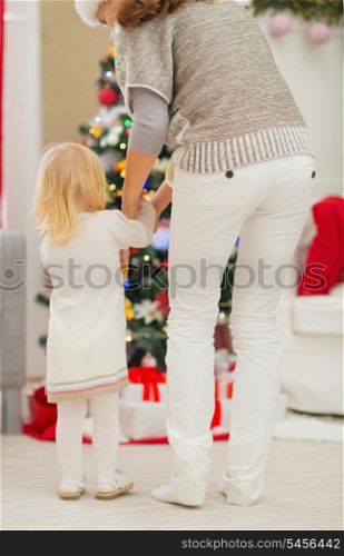 Baby and mother in front of Christmas tree. Rear view