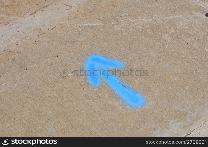 Baby blue arrow pointint northwest on concrete