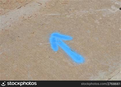 Baby blue arrow pointint northwest on concrete