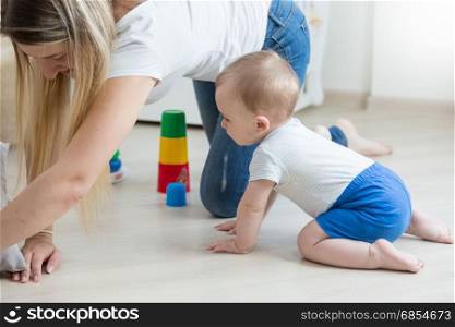 Baby boy crawling on floor and assembling toy tower with mother