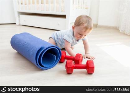 Baby boy crawling on floor and playing with dumbbells