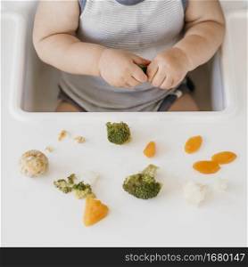 baby boy highchair eating vegetables alone