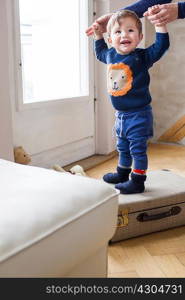 Baby boy holding mothers hands and standing on suitcase