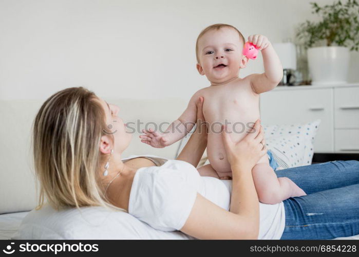 Baby boy in diaper sitting on mother lying on bed