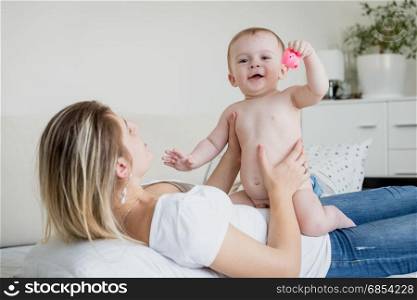 Baby boy in diaper sitting on mother lying on bed