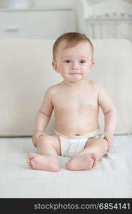 Baby boy in diapers sitting on bed and holding smartphone