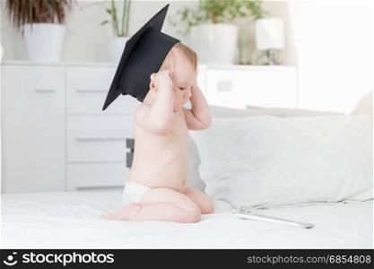 Baby boy in graduation cap looking at digital tablet