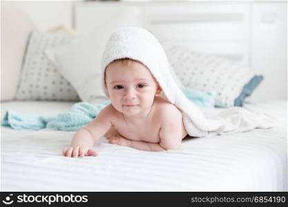 Baby boy in hooded towel crawling on bed after having bath