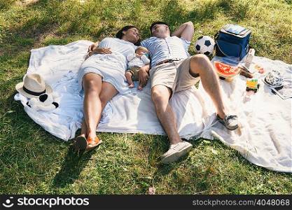 Baby boy lying between parents on picnic blanket in Pelham Bay Park, Bronx, New York, USA