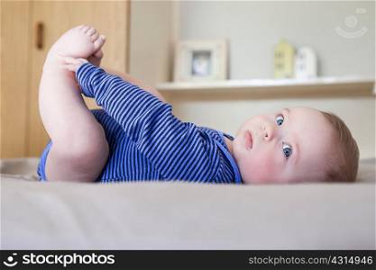 Baby boy lying on bed playing with his feet