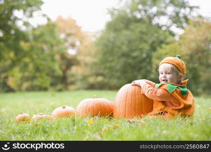 Baby boy outdoors in pumpkin costume with real pumpkins