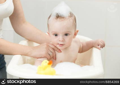 Baby boy playing in foam bath with yellow rubber duck